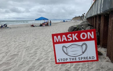 sign reading "Mask On - stop the spread" at the beach